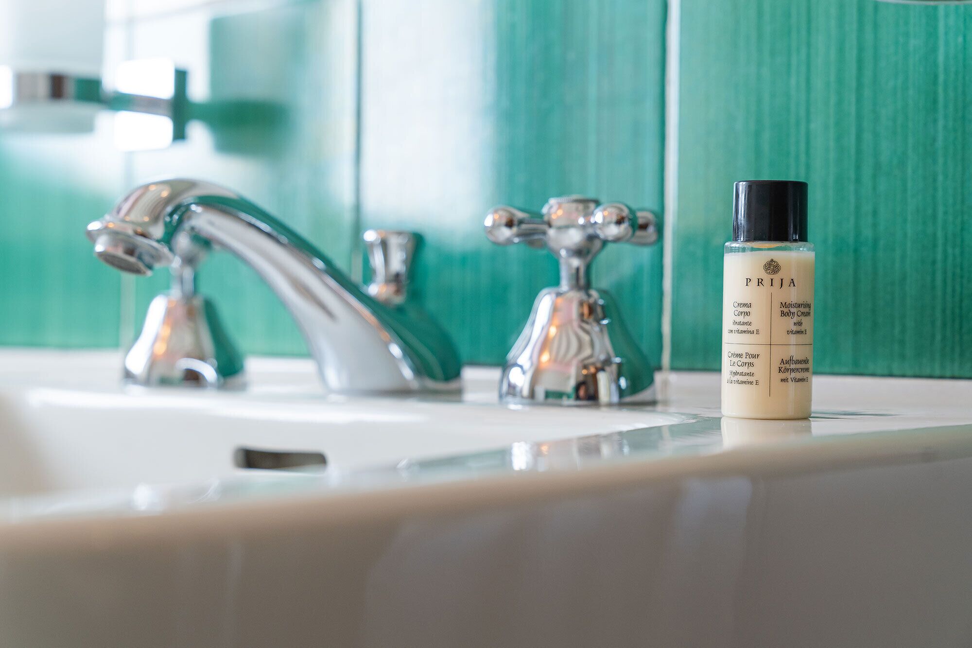 A bathroom sink with a modern faucet and a bottle of body cream labeled "PRIJA" on the counter.