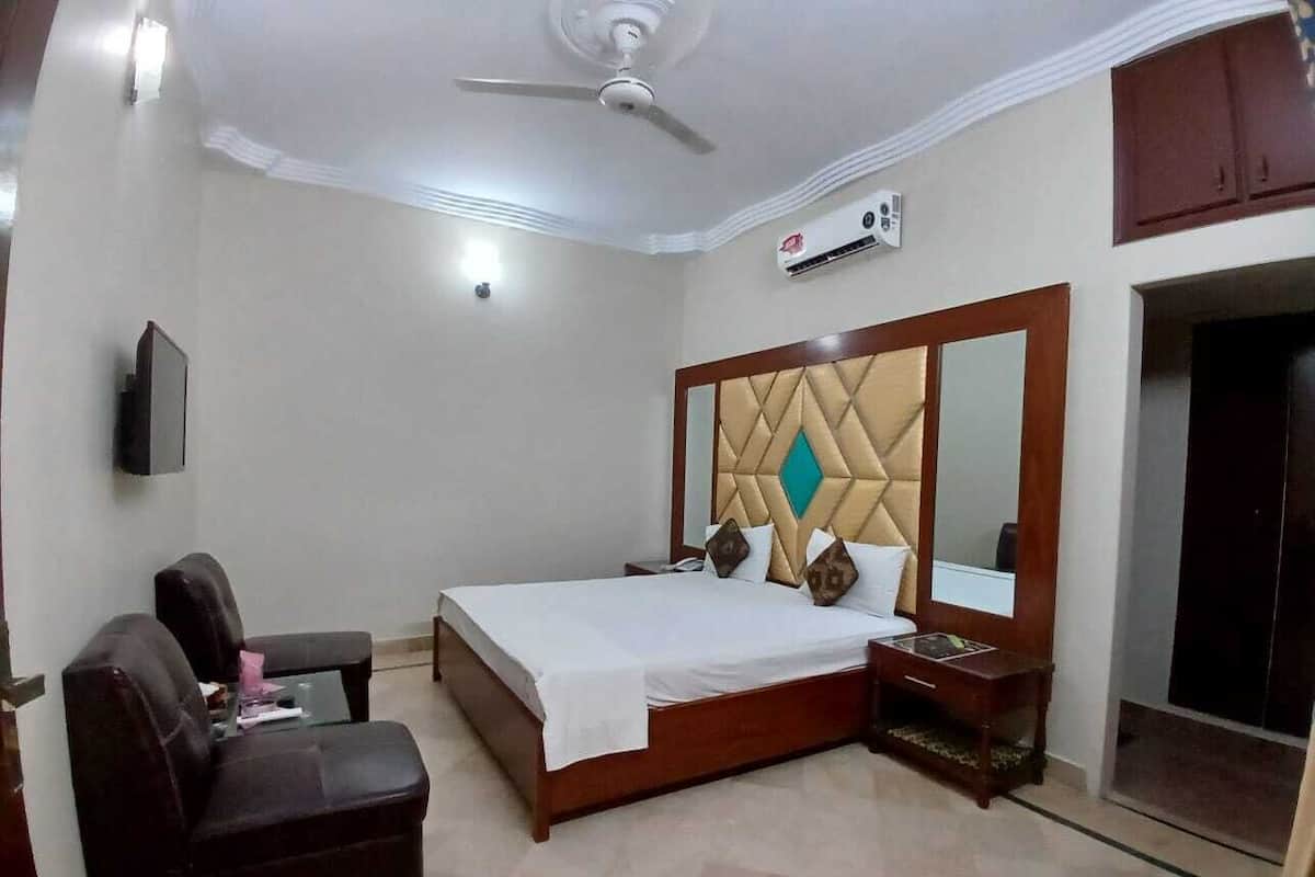 A hotel room with a bed, a desk, a chair, a mirror, and a ceiling fan.