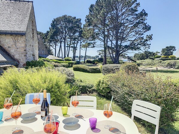 A table set for a meal with wine glasses and a bottle, surrounded by greenery and trees.