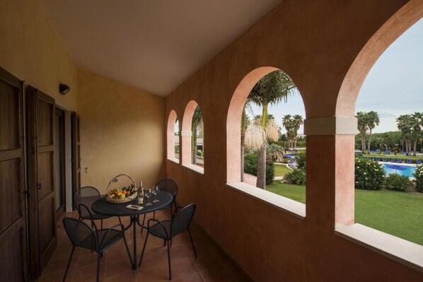 A balcony with a table and chairs, a view of a pool and palm trees.