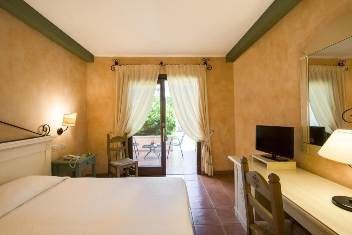 Habitación de hotel con cama, escritorio, televisión y vistas a un patio exterior.