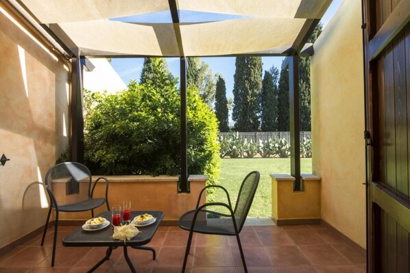 A covered patio with a table set for two, chairs, and a view of the garden.