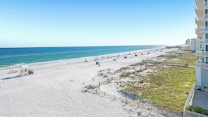 Ein Strand mit sandigem Ufer, einer Holzlattenzaun und einem Gebäude mit mehreren Balkonen.