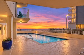 Una piscina en la azotea con vistas al atardecer, un balcón y un edificio moderno al fondo.