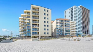 Ein Strandhotel mit mehreren Balkonen und einem sandigen Strand im Vordergrund.