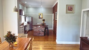 A modern kitchen with a brick island, wooden dining table, and chairs. - The BnB filled to the brim with character and charm! (Dubbo)