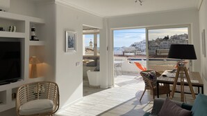 A modern living room with a TV, seating, a dining area, and a balcony with a city view.