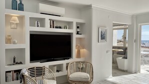 A modern living room with a large flat-screen TV, wicker chairs, and built-in shelving with decorative items.