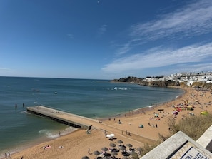 A beach with a pier extending into the water, people on the sand, and buildings in the background.