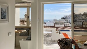 A balcony with a view of a coastal cityscape, a dining area with a table and chairs, and a framed picture on the wall.