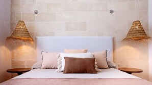 A bedroom with a large bed, two bedside tables, and a textured wall. - Appartamento Cala Rotonda (Favignana)