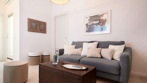 A living room with a grey sofa, a round ottoman, a wooden coffee table, and two wall-mounted baskets. - Appartamento Cala Rotonda (Favignana)