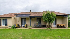 Une maison avec un toit en tuiles, un patio couvert avec des meubles d’extérieur et une pelouse bien entretenue.