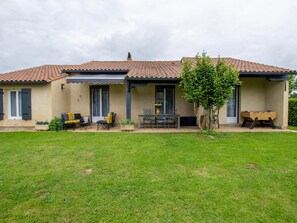 Una casa amb teulada de rajola, una terrassa coberta amb mobles d'exterior i un jardí ben cuidat.