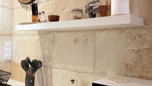 Eine Küche mit weißer Arbeitsplatte, einer Pendelleuchte und einem Regal mit Küchenutensilien und einer Kaffeemaschine.