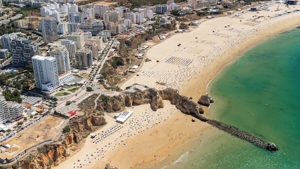 Vue aérienne d’une ville côtière avec de hauts immeubles, une plage de sable et un promontoire rocheux.
