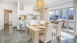 Un appartement moderne doté d’un coin repas, d’une cuisine et de grandes fenêtres offrant une vue sur la ville.
