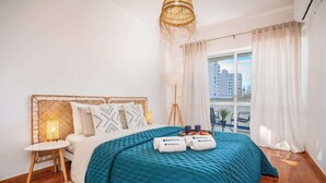 Une chambre à coucher moderne avec un grand lit, une table de chevet, une lampe et une vue sur la ville par la fenêtre.
