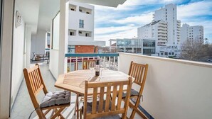 Un balcon avec une table et des chaises en bois, donnant sur un paysage urbain avec des bâtiments modernes.