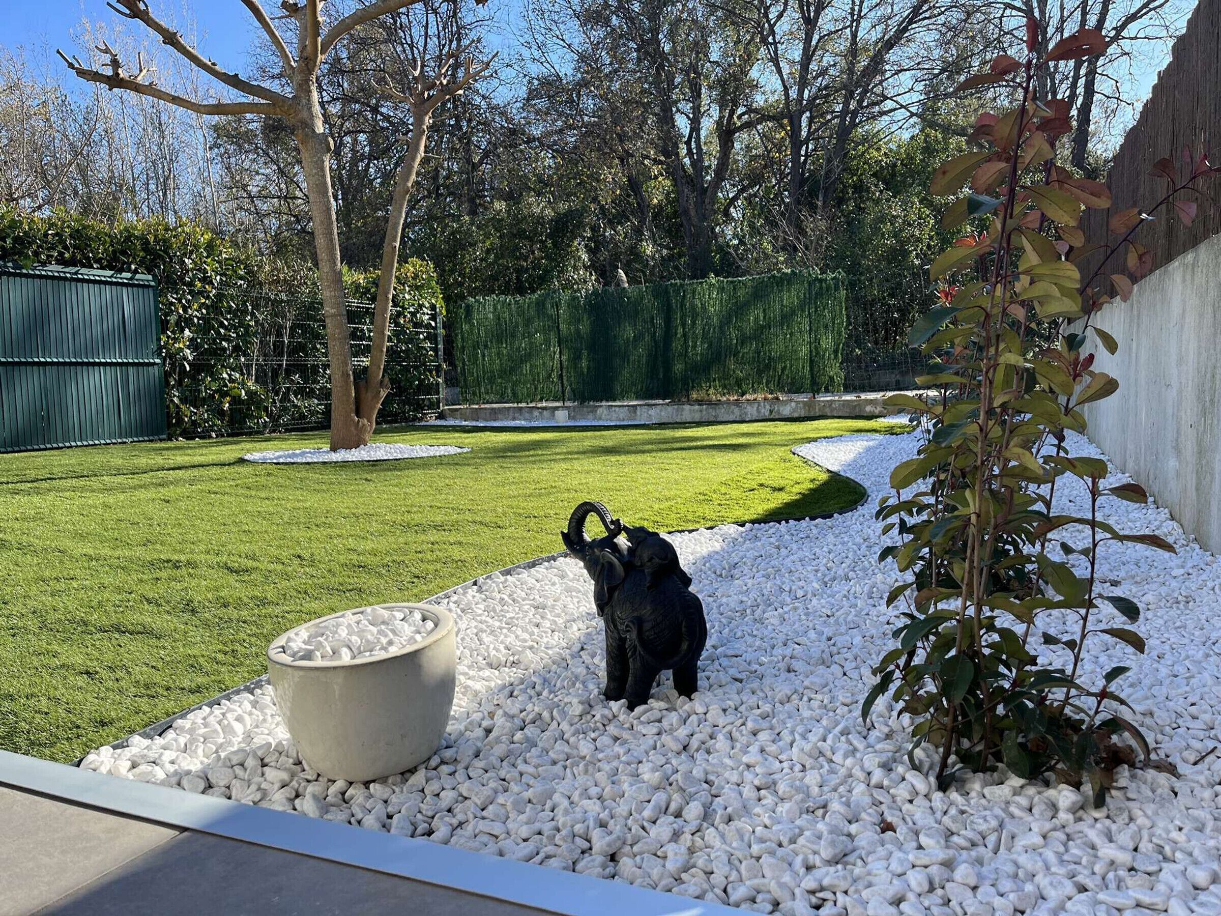 Ein Garten mit einer Bärenstatue, einem großen Pflanzgefäß und einer Hecke.