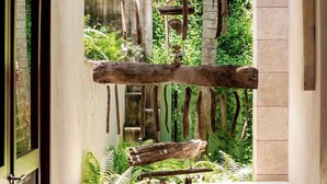 A modern interior with a wooden structure hanging from the ceiling, a concrete wall, and a view of greenery outside. - Casa Colmena: Luxury 6BR Villa w/ Infinity Pool (Corral del Risco)