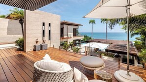 A modern outdoor deck with wooden flooring, wicker furniture, and a view of the ocean. - Casa Colmena: Luxury 6BR Villa w/ Infinity Pool (Corral del Risco)