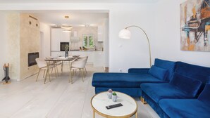 A modern living room with a blue sofa, a round coffee table, and a dining area with a white table and chairs. - Emerald Eco Villa (Povlja)