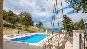A pool area with a swing chair, lounge chairs, and a view of the landscape. - Emerald Eco Villa (Povlja)
