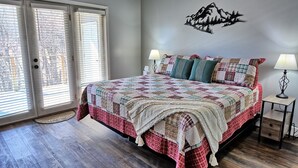 Een slaapkamer met een groot bed, twee bedlampjes, een kunstwerk aan de muur, en uitzicht door de deur.