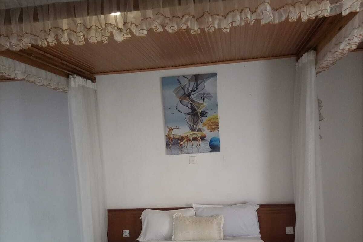 A bedroom with a wooden bed, white bedding, a painting on the wall, and a patterned floor.