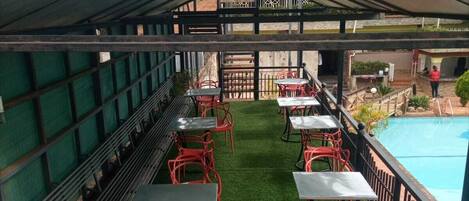 An outdoor seating area with tables and chairs, a pool, and a covered section with a roof.