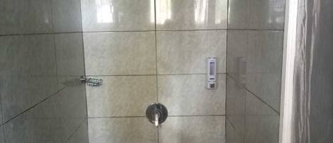 A shower stall with a handheld showerhead, a control panel, and a tiled floor.