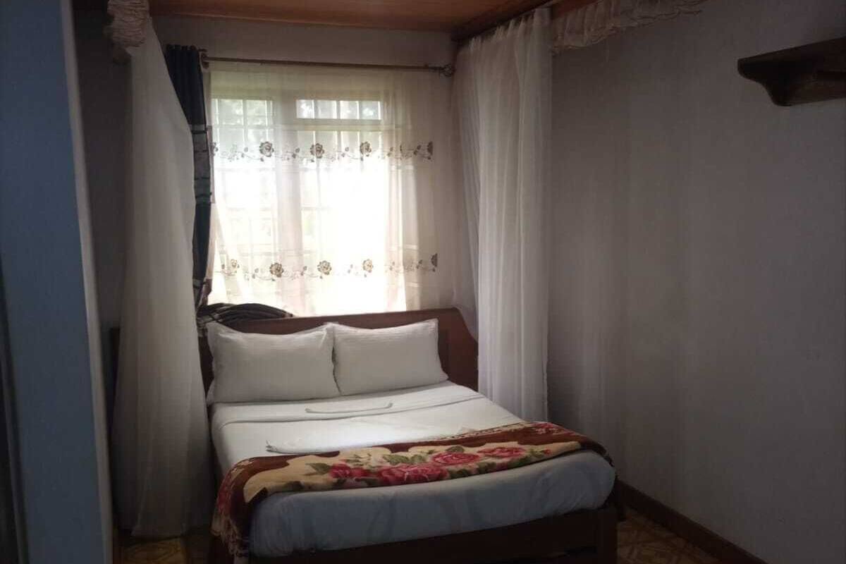 A single bed with a floral bedspread, a wooden headboard, and a window with sheer curtains.