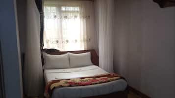 A single bed with a floral bedspread, a wooden headboard, and a window with sheer curtains.