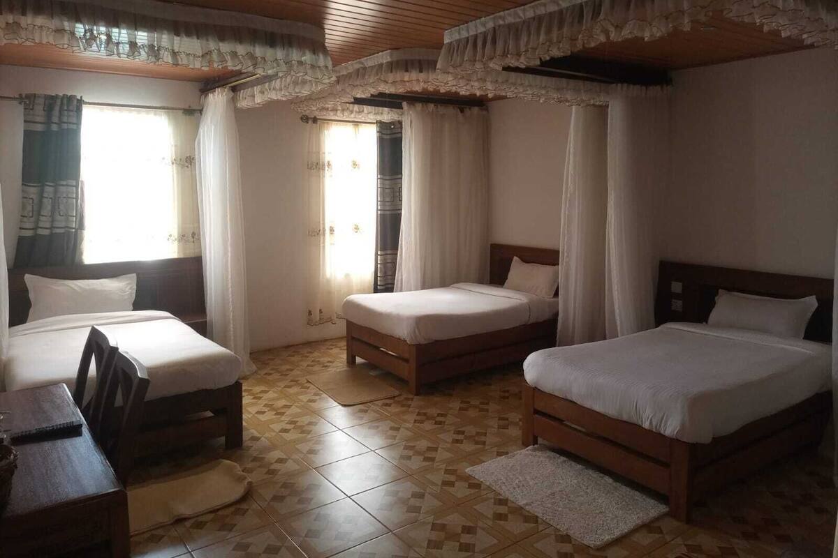 A hotel room with three beds, a wooden ceiling, and a tiled floor.