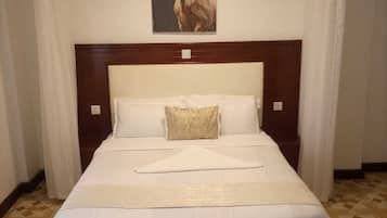 Cama bem arrumada com cabeceira de madeira, roupa de cama branca e almofada decorativa.