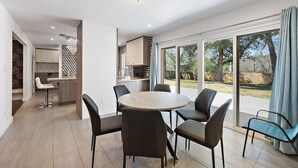 Een moderne keuken met een centraal eiland, een eethoek met zes stoelen en een grote glazen schuindeur die uitkomt op een achtertuin.