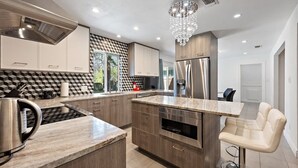 Een moderne keuken met een centraal eiland, roestvrijstalen apparatuur en een kroonluchter.