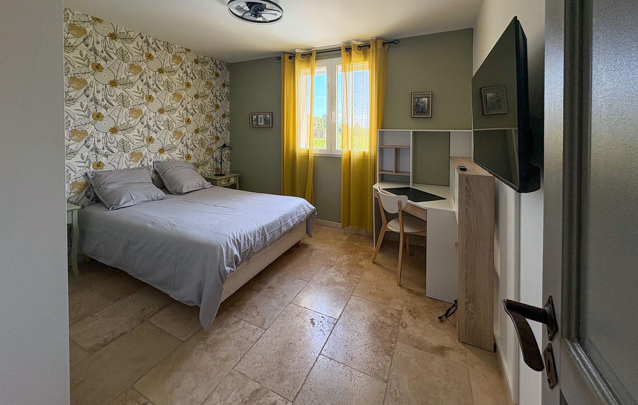 Een slaapkamer met een bed, een bureau, een stoel en een televisie aan de muur.