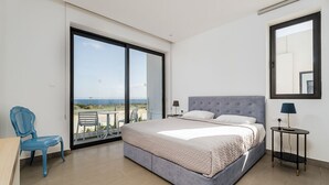 A bedroom with a large bed, a chair, a small table, and a balcony with a view. - Villa Ektoras at Periyiali Resort with  modern design, and amenities.  (Paralimni)