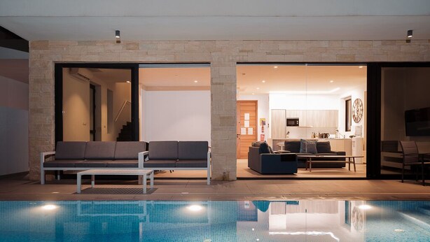 A modern indoor swimming pool area with a seating area and a kitchen visible through an open doorway. - Villa Ektoras at Periyiali Resort with  modern design, and amenities.  (Paralimni)