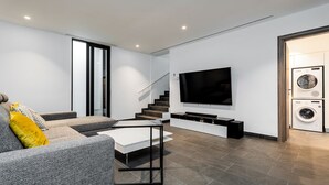 A modern living room with a grey sofa, a coffee table, a flat-screen TV, a staircase, and a washing machine. - Villa Ektoras at Periyiali Resort with  modern design, and amenities.  (Paralimni)
