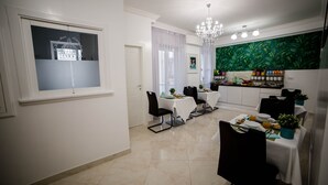Zona pranzo con vista su un edificio attraverso una finestra, un lampadario e una cucina con un affresco tropicale.