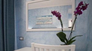 Una stanza modesta con una scrivania bianca, un frigorifero nero, una televisione montata a parete e un quadro incorniciato sopra la scrivania.