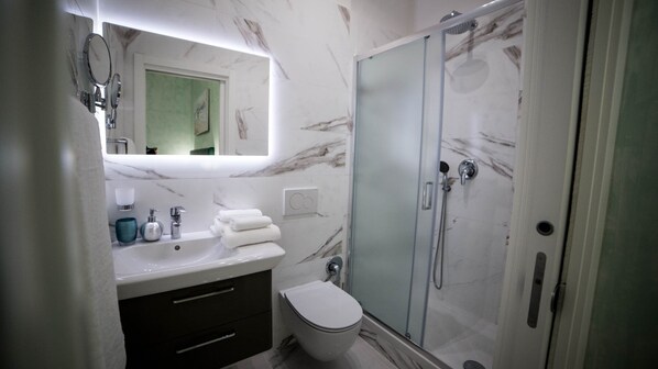 A modern bathroom with a marble sink, a toilet, and a glass-enclosed shower. - St. Peter Area Luxury Suites (Rome)