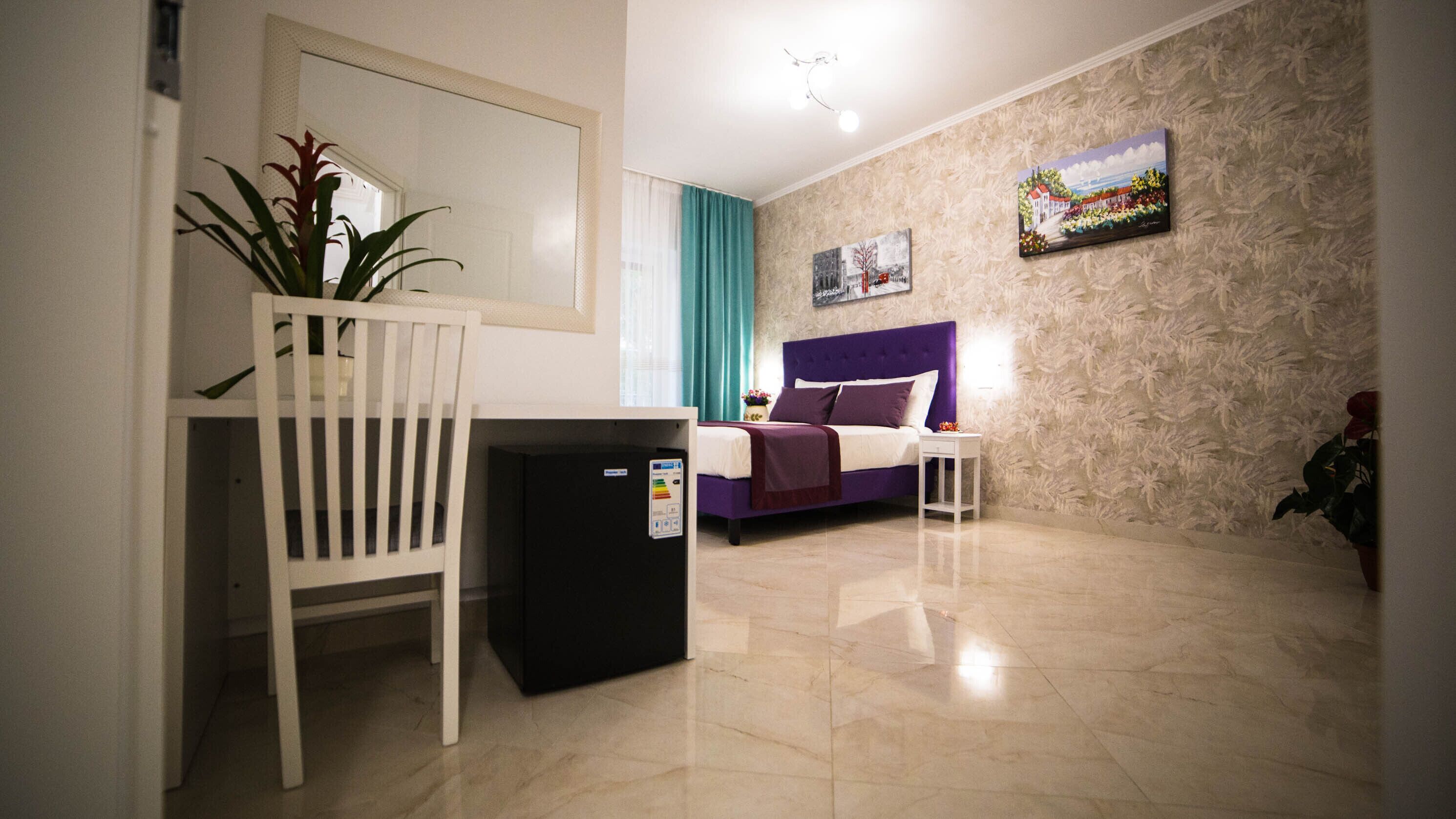 Quarto de hotel com cama, pequena mesa de trabalho, cadeira, frigorífico e um quadro na parede.