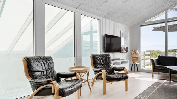 A modern living room with large windows, a flat-screen TV, leather chairs, a small table, and a view of the outdoors. - Nice home in Hvide Sande with sauna (Hvide Sande)