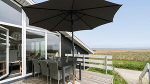 A deck with a table and chairs, a large umbrella, and a view of the beach. - Nice home in Hvide Sande with sauna (Hvide Sande)