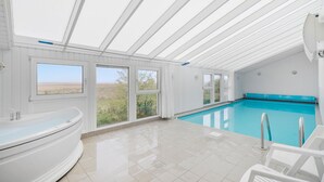 A modern indoor swimming pool with a clear view of the outdoors through large windows. - Nice home in Hvide Sande with sauna (Hvide Sande)