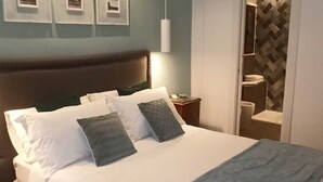 A neatly made bed with white and gray bedding, a wooden headboard, and a nightstand with a lamp. - Jacona 365 Apartment - In the historic center area of Palermo. (Palermo)